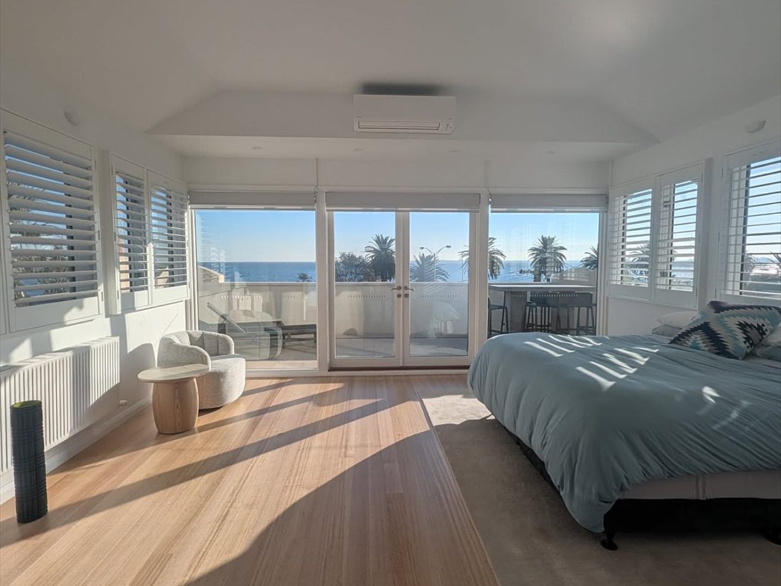 Master bedroom with white walls and plantation shutters opening onto an ocean view