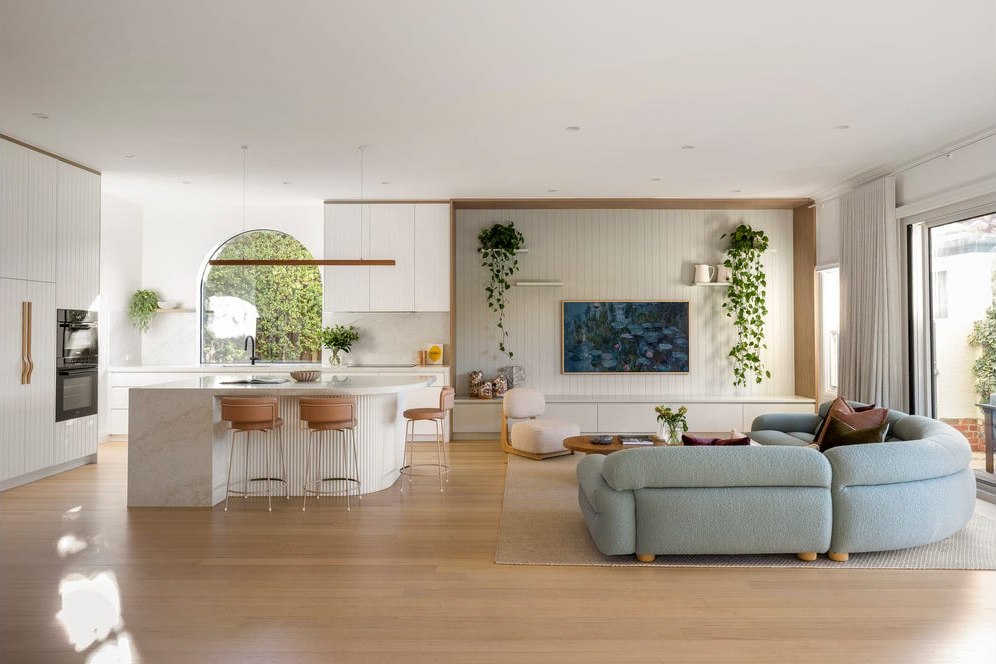 Open-plan kitchen and living room in white, with a stone island bench, timber floors and sliding doors to a terrace